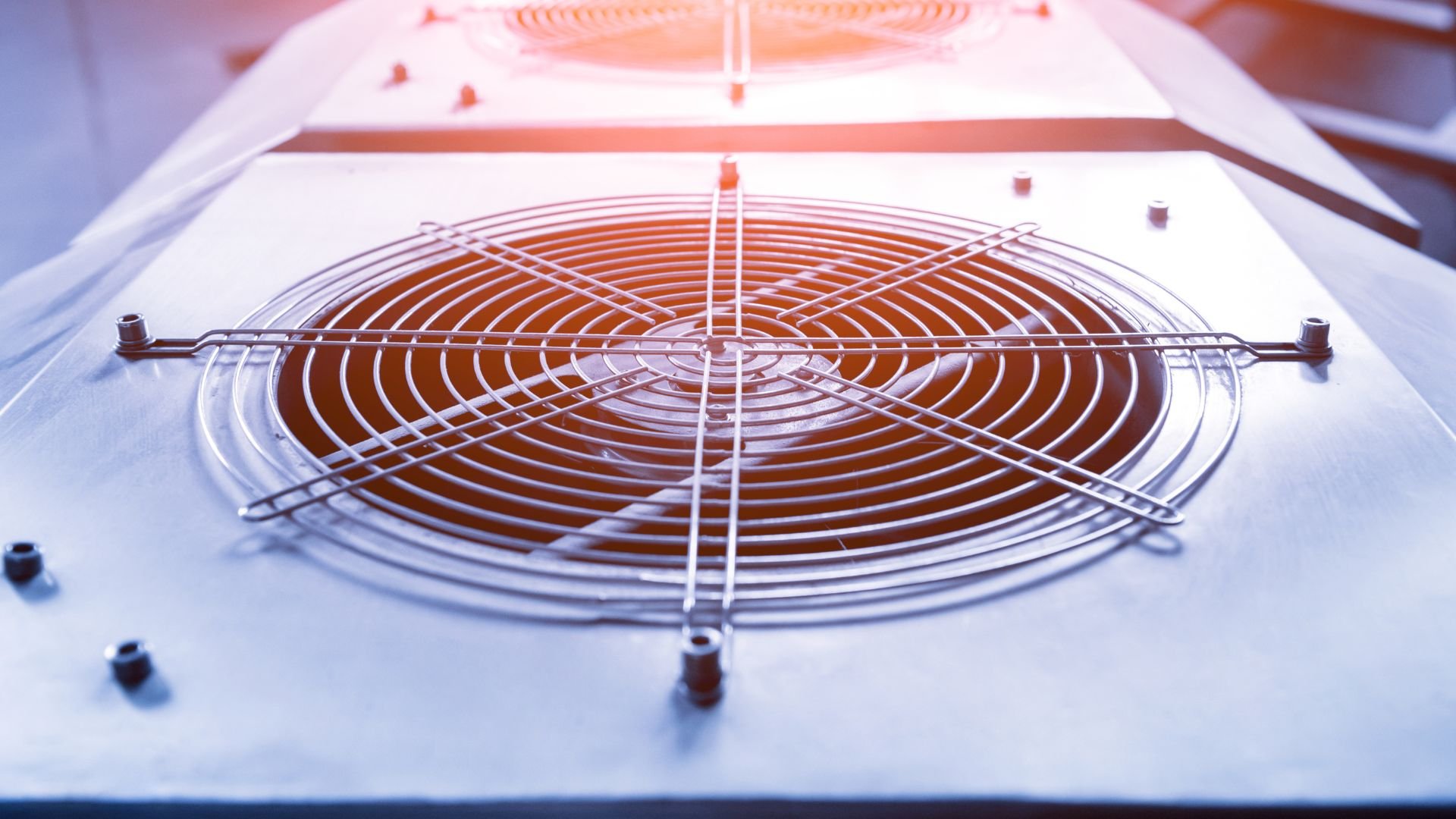Industrial cooling fan with metal grate against blue-white background
