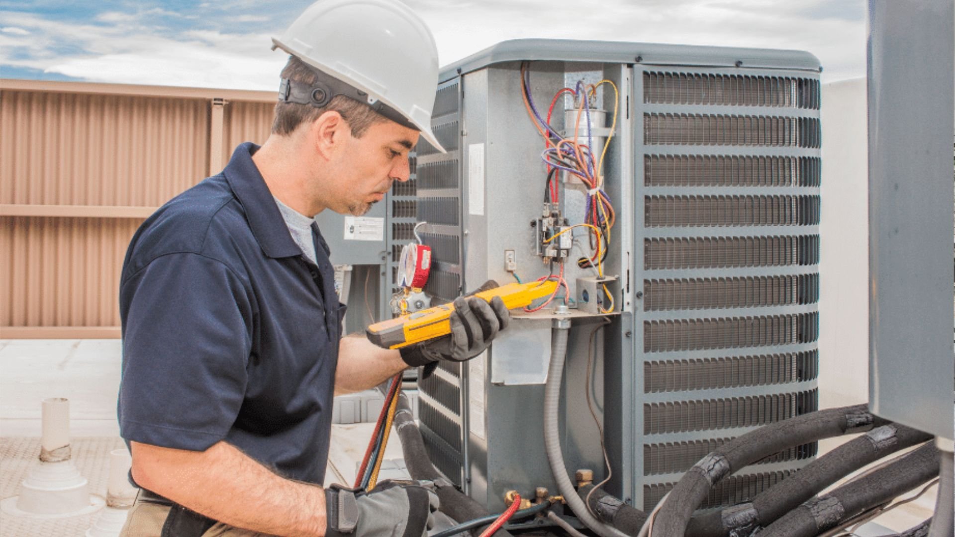 Technician in hard hat checking electrical connections on HVAC unit